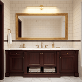 Gold rod lit above a gilt framed mirror over a dark wood vanity unit