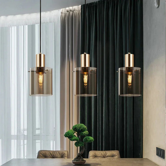 Three copper pendants in a row lit in front of a dark green curtain