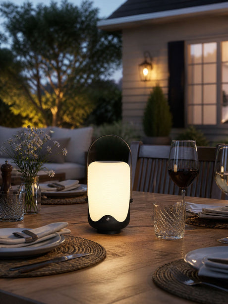 The lamp lit on a laid dinner table outdoors with glasses and plates