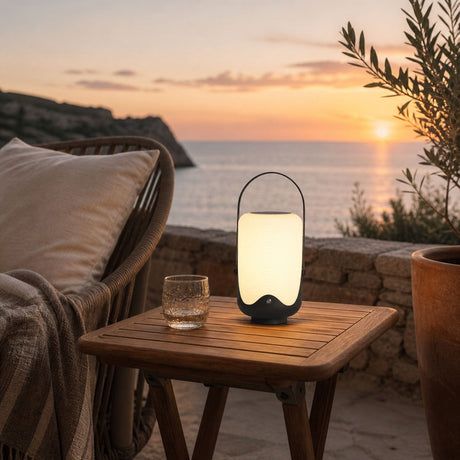The lamp lit on a timber side table on a terrace above the sea at sunset