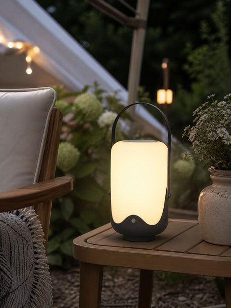 The lamp lit on a side table beside a chair and a bowl of hydrangeas