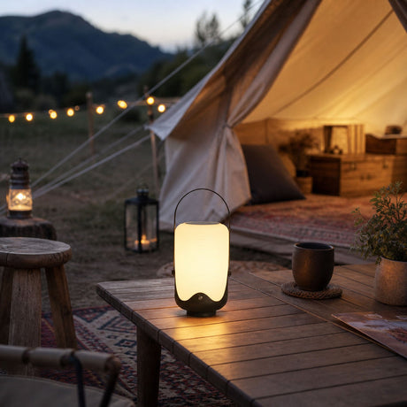 The lamp lit on a table beside a canvas tent with a rug and a lantern