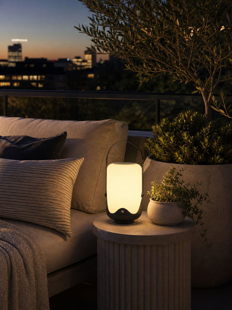 The lamp lit on a bench with cushions and planters on a city terrace