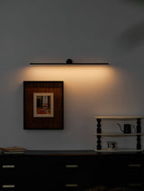 Black bar lit above a framed print on a dark wall, warm light washing down it