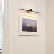 Black bar lit above a framed photograph on a white wall beside a door frame