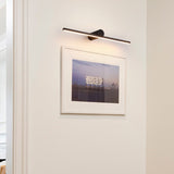 Black bar lit above a framed photograph on a white wall beside a door frame