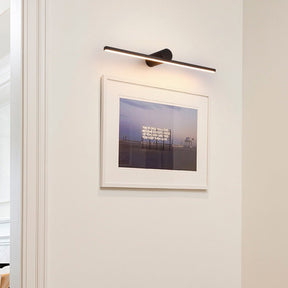Black bar lit above a framed photograph on a white wall beside a door frame