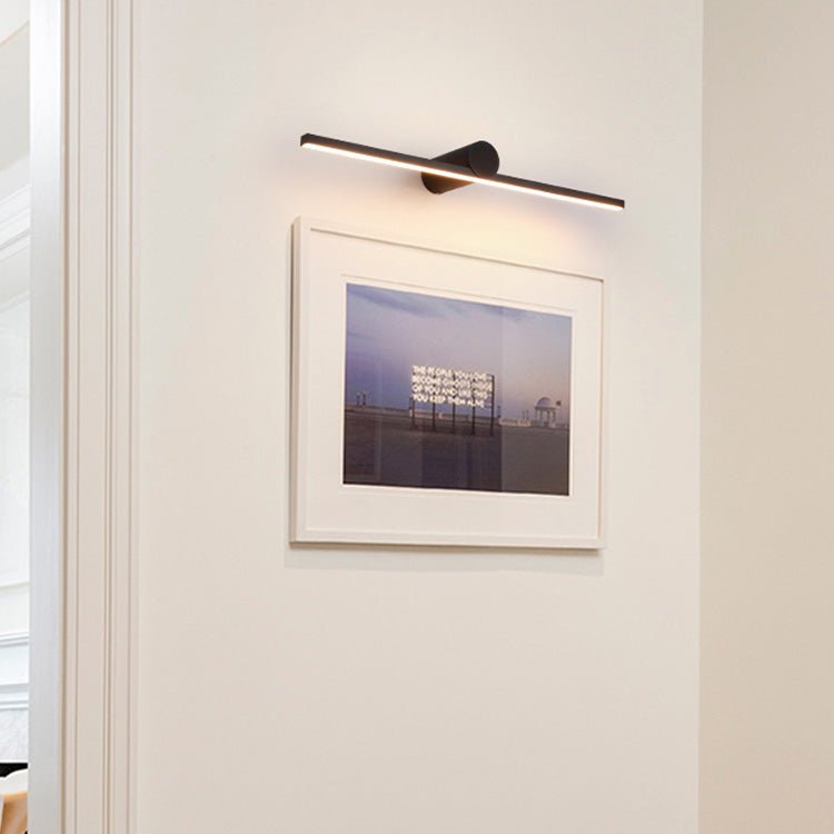 Black bar lit above a framed photograph on a white wall beside a door frame
