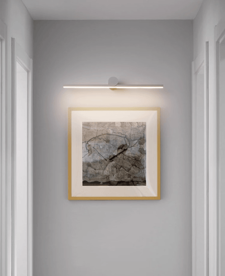 Black bar lit above a gilt framed landscape in a narrow hallway beside a doorway
