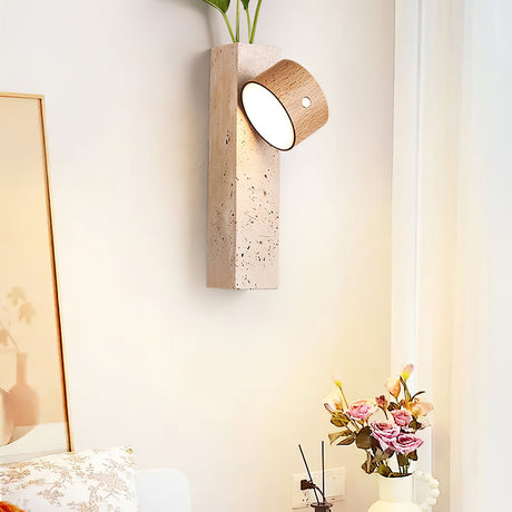 Wall sconce lit on a pale wall next to a window and a vase of flowers