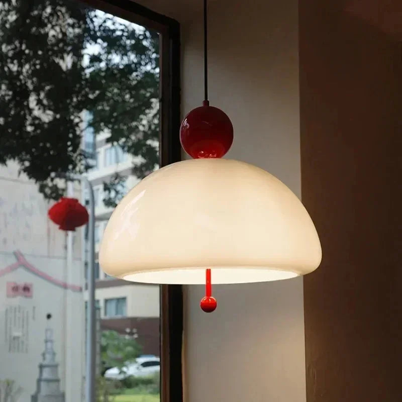 The cream glass dome with a red knob lit beside a window and a wooden wall