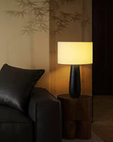 Cream table lamp lit beside a dark leather sofa and cushion