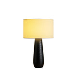 Cream table lamp on a black turned base, lit on a plain ground