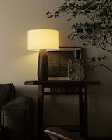 Cream table lamp lit on a console beside a framed artwork
