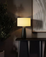 Cream table lamp lit on a dark console below a framed picture