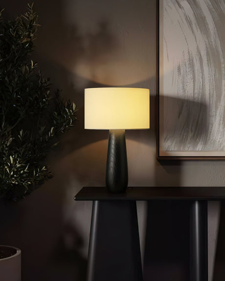 Cream table lamp lit on a dark console below a framed picture