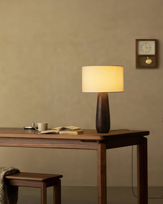 Cream table lamp lit on a wood desk beside an open notebook