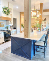 Two of them lit above a blue kitchen island with stools and a range beyond