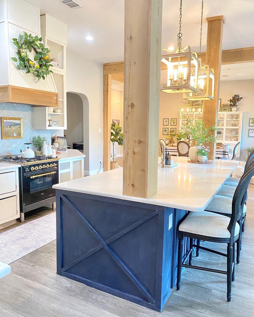 Two of them lit above a blue kitchen island with stools and a range beyond
