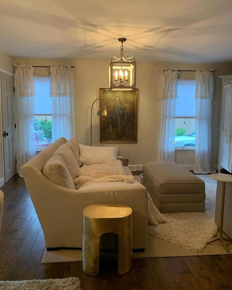 Lit in a living room between two windows above a sofa with artwork behind