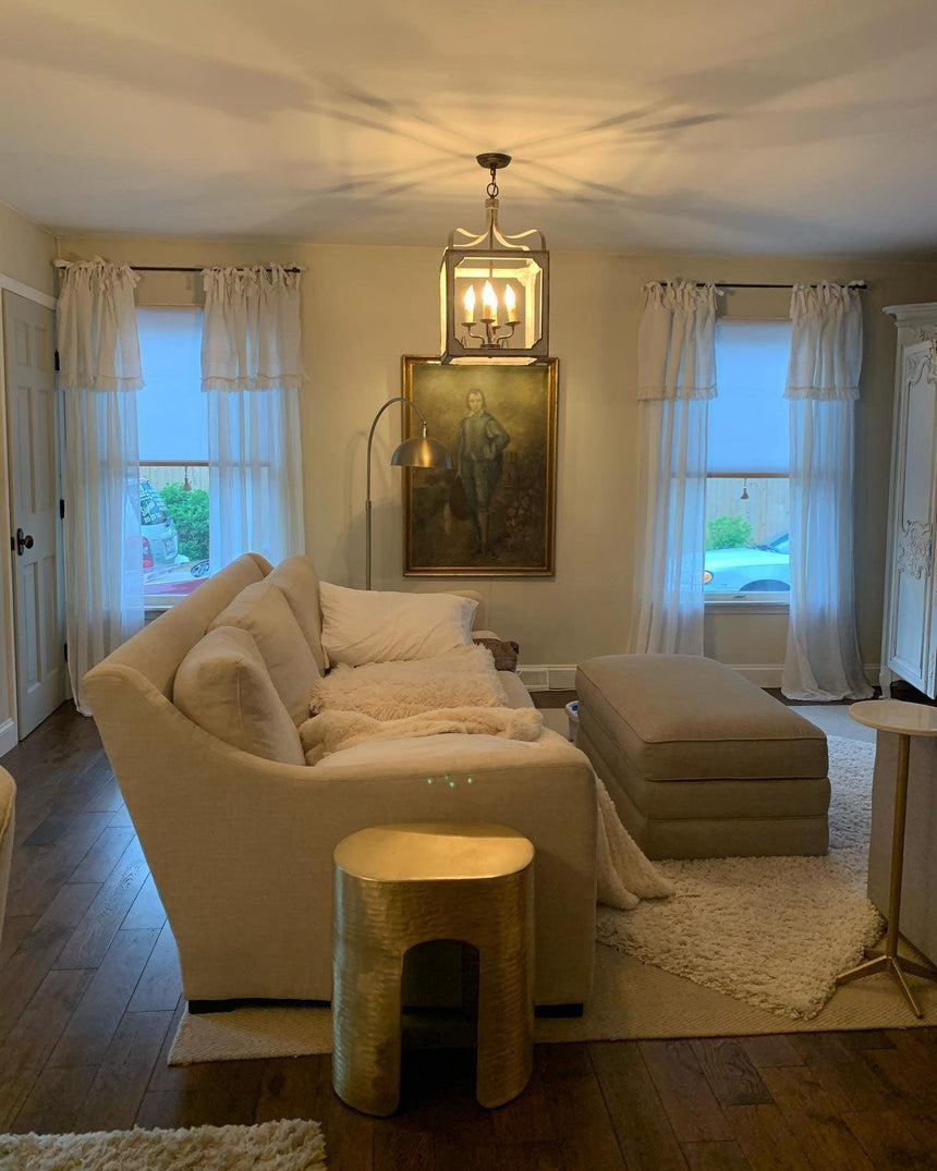 Lit in a living room between two windows above a sofa with artwork behind