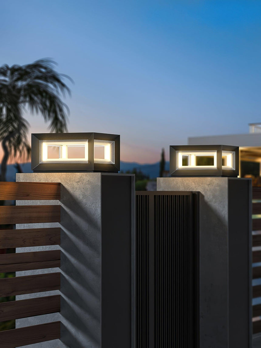 The cubes lit on two pillars beside a fence panel at dusk