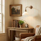 The sconce above a wood console with books and a clock beside a leather armchair