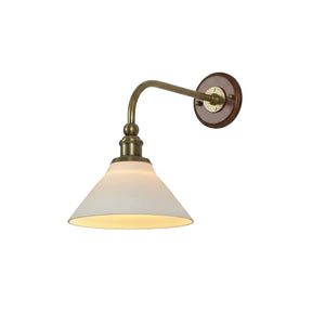 Wall sconce with a curved brass arm, a round wood wall plate and a white cone shade