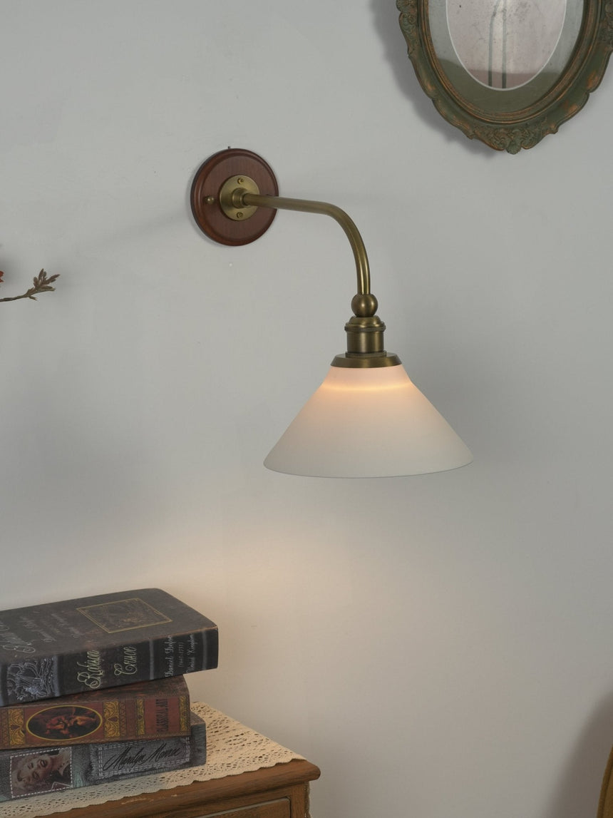 The sconce lit on a pale wall above a stack of old books
