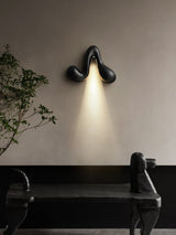 Sconce lit above a dark bench beside a branch in a tall floor vase