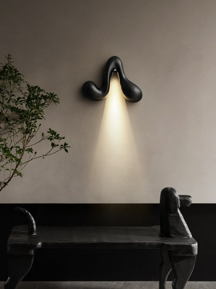 Sconce lit above a dark bench beside a branch in a tall floor vase