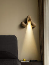 Sconce lit beside a long curtain above a headboard and a side table