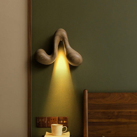 Sconce lit on a green wall beside a wood headboard and a bedside cup