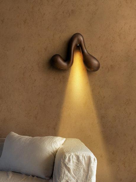 Sconce lit above a pale sofa with cushions against a plaster wall