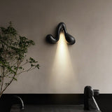 Sconce lit beside a slim plant above a dark bench in a quiet corner
