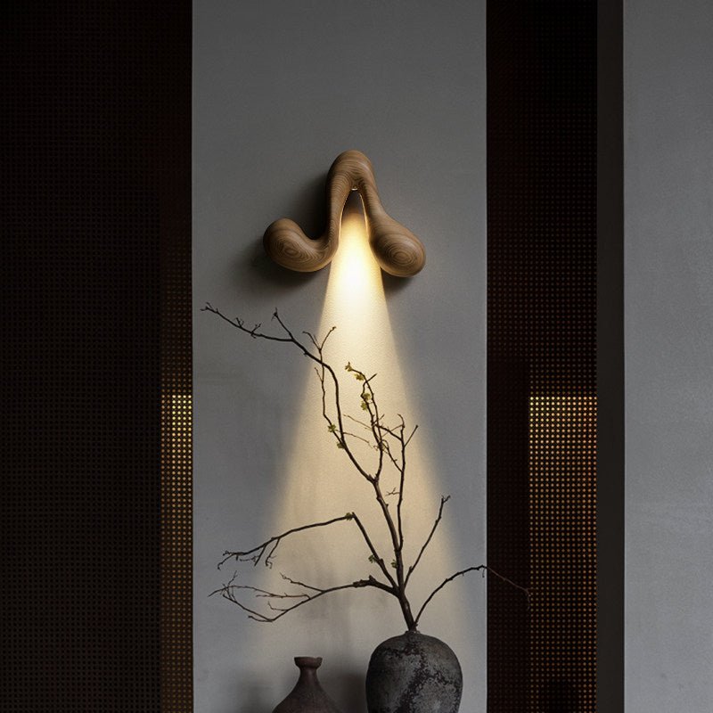 Sconce lit above a stone vase of bare branches against a dark panel