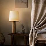 Cylinder table lamp lit on a console beside a linen curtain