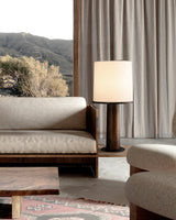 Cylinder table lamp lit on a side table beside a pale sofa