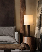 Cylinder table lamp lit in a lounge beside a low sofa and timber