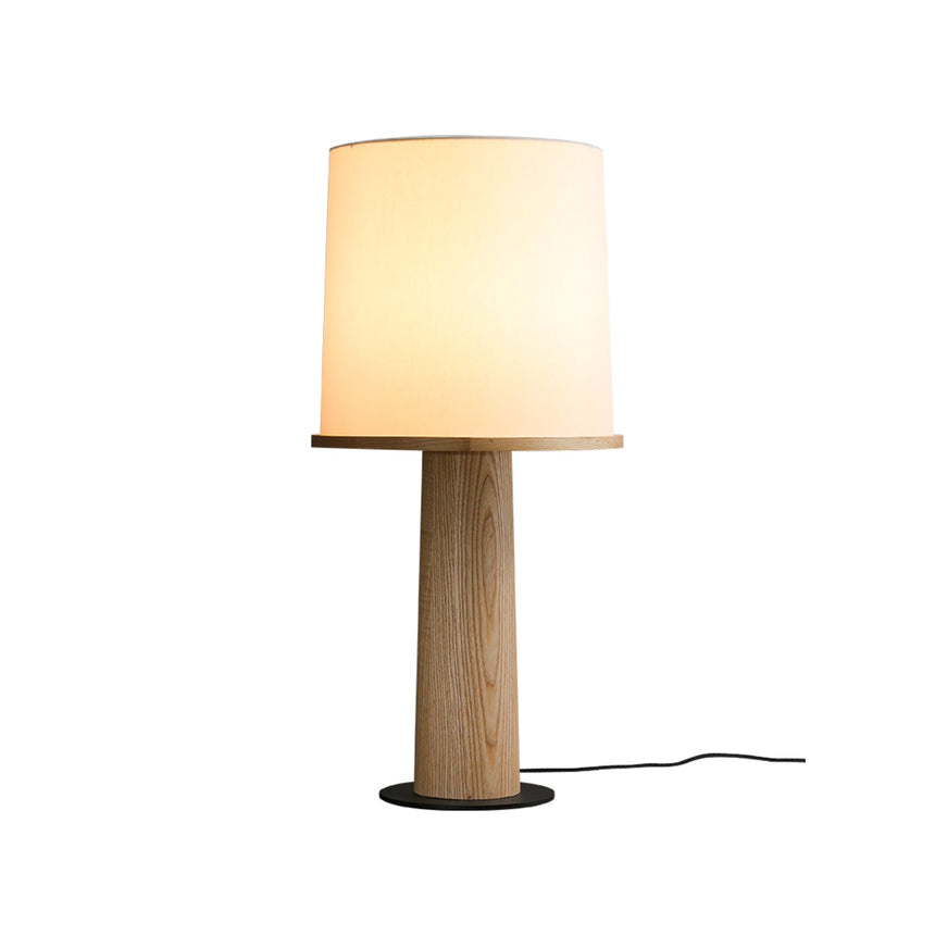 Light wood cylinder table lamp lit against a plain pale ground