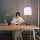 Cylinder table lamp lit on a long desk while someone reads