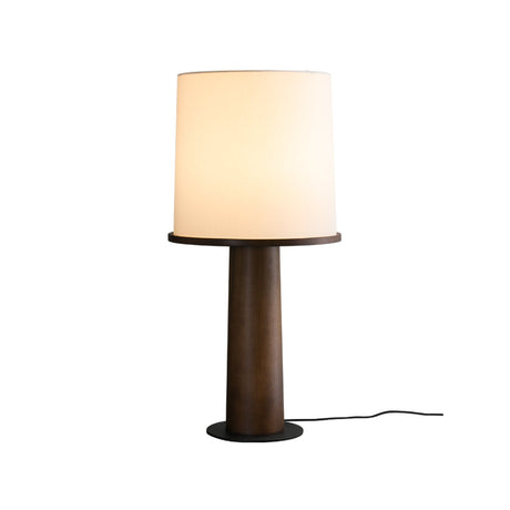 Walnut cylinder table lamp lit against a plain pale ground