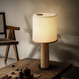 Cylinder table lamp lit on a wood table beside a dark tea set