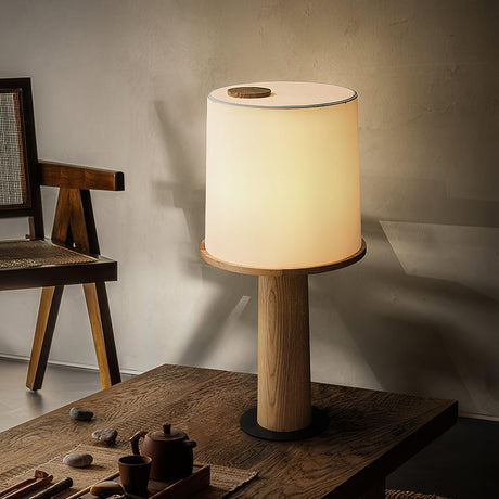 Cylinder table lamp lit on a wood table beside a dark tea set