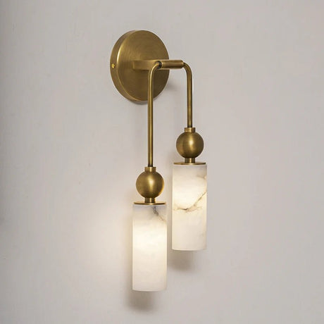 Two lit stone cylinders hanging from curved brass arms on a pale wall