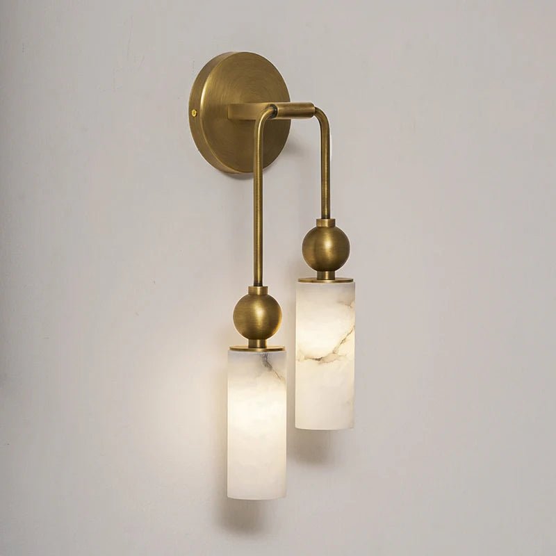 Two lit stone cylinders hanging from curved brass arms on a pale wall