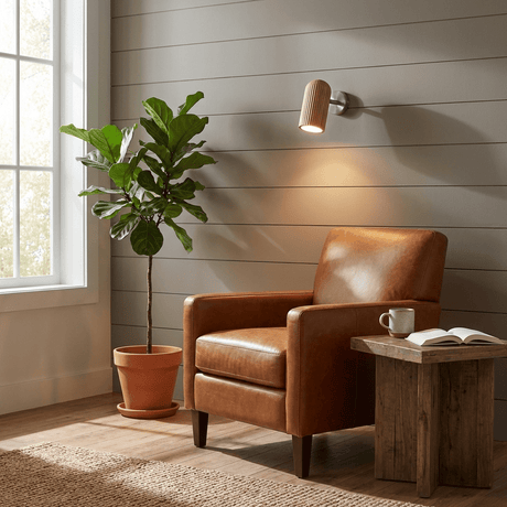 Sconce lit above a leather armchair beside a potted plant and a window