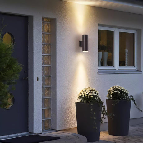 A cylinder light beside a dark front door and glass blocks, potted flowers below