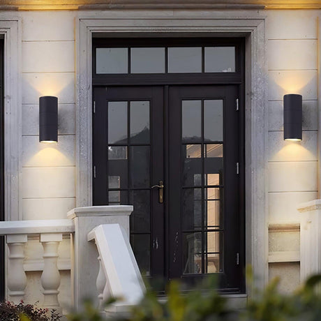 Two cylinder lights flanking a double glass door on a stone facade