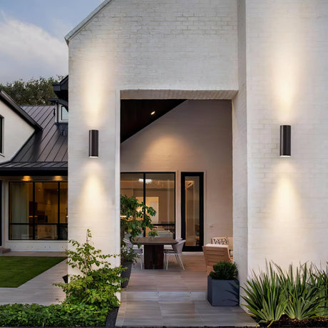 Cylinder lights on a white brick house either side of a covered patio with a dining table